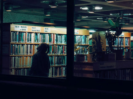Una persona in controluce sfoglia dei libri in una libreria scarsamente illuminata.