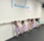 Young girls in pastel ballet outfits practicing tap dance at a dance barre at Tamraloo Studios with the words "Tamraloo Dance" on the wall.