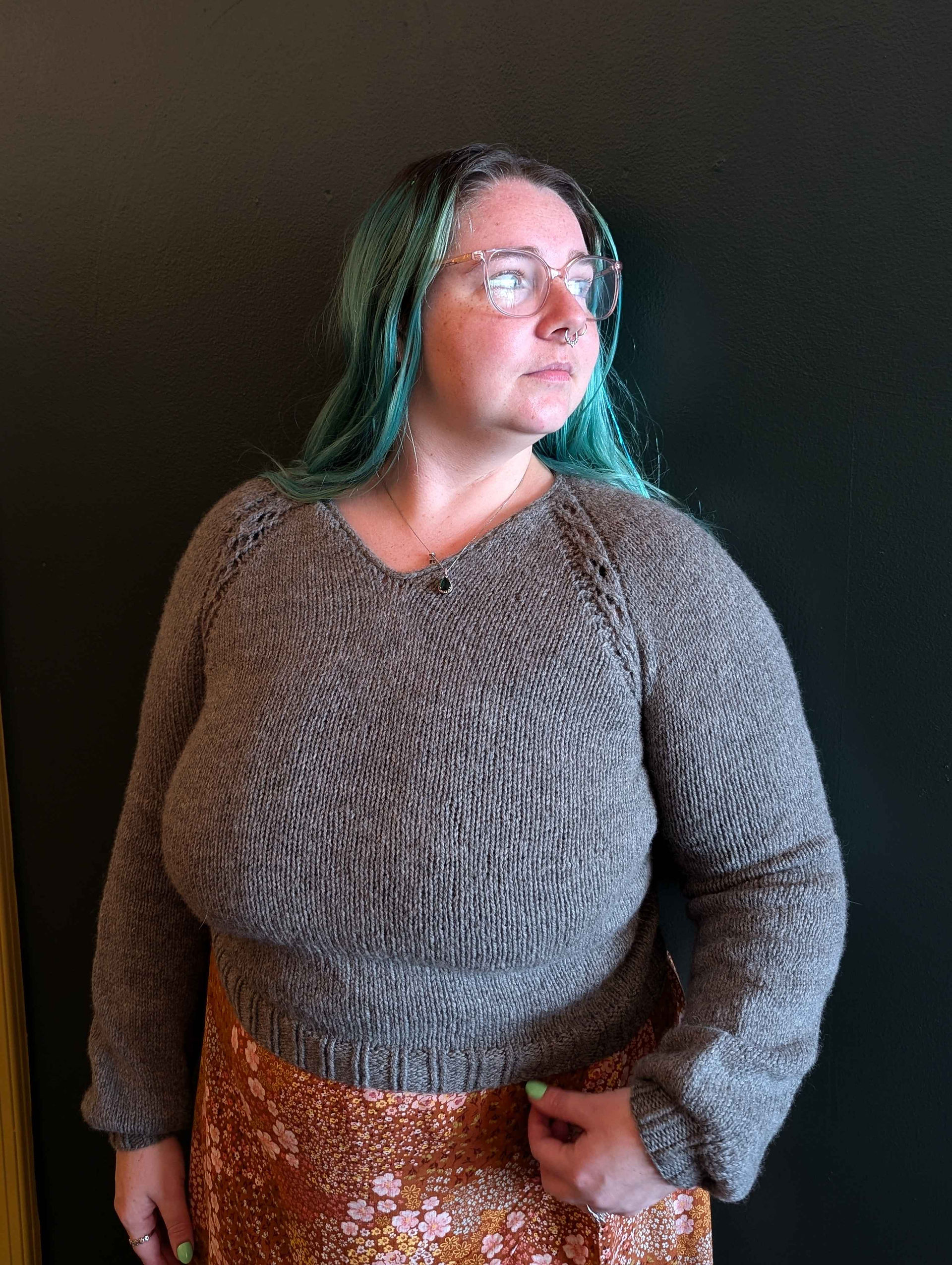 Woman wearing a grey Stolen Silver Spoons crop looks to the side while standing in front of a plain dark background. 