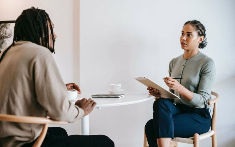 Therapist listening attentively and making notes while speaking with a client during a counseling session.