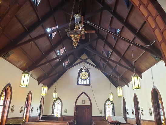 Interior of the 19th Century Gothic Chapel with arched stained glass windows, stained glass trancepts, original pews, white walls and Gothic style arched entry door