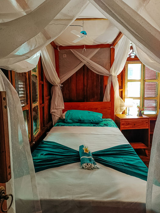 Double bedroom in Zinnia at Alaya Ecolodge, Pemuteran, featuring teal bedding and wooden decor.
