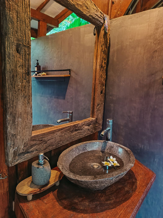 Stone basin and rustic wooden mirror in the bathroom at Marigold Cottage, Pemuteran.