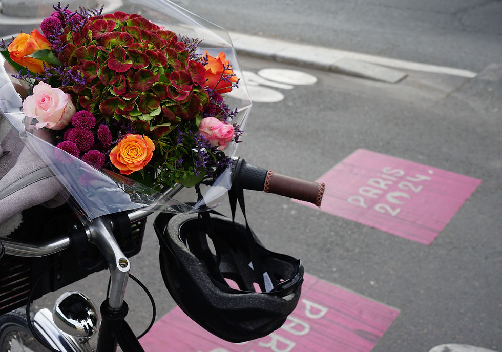 Close-up of a bouquet of flowers in the basket of a bike, with the bike positioned on a bike lane marked 'Paris 2024.