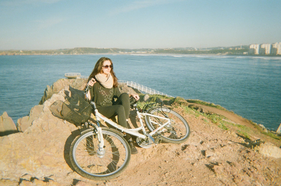 Bea holding a bike on a cliff overlooking the sea in sunny Salinas, Spain.