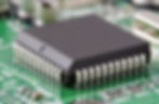 Gambar: Chip IC berbentuk persegi dengan pin logam di kedua sisi terpasang pada PCB hijau.