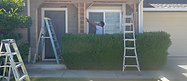 Handyman removing a small exterior wall section between a front door and window.