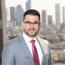 A man in a suit smiling in front of a window with a red tie.