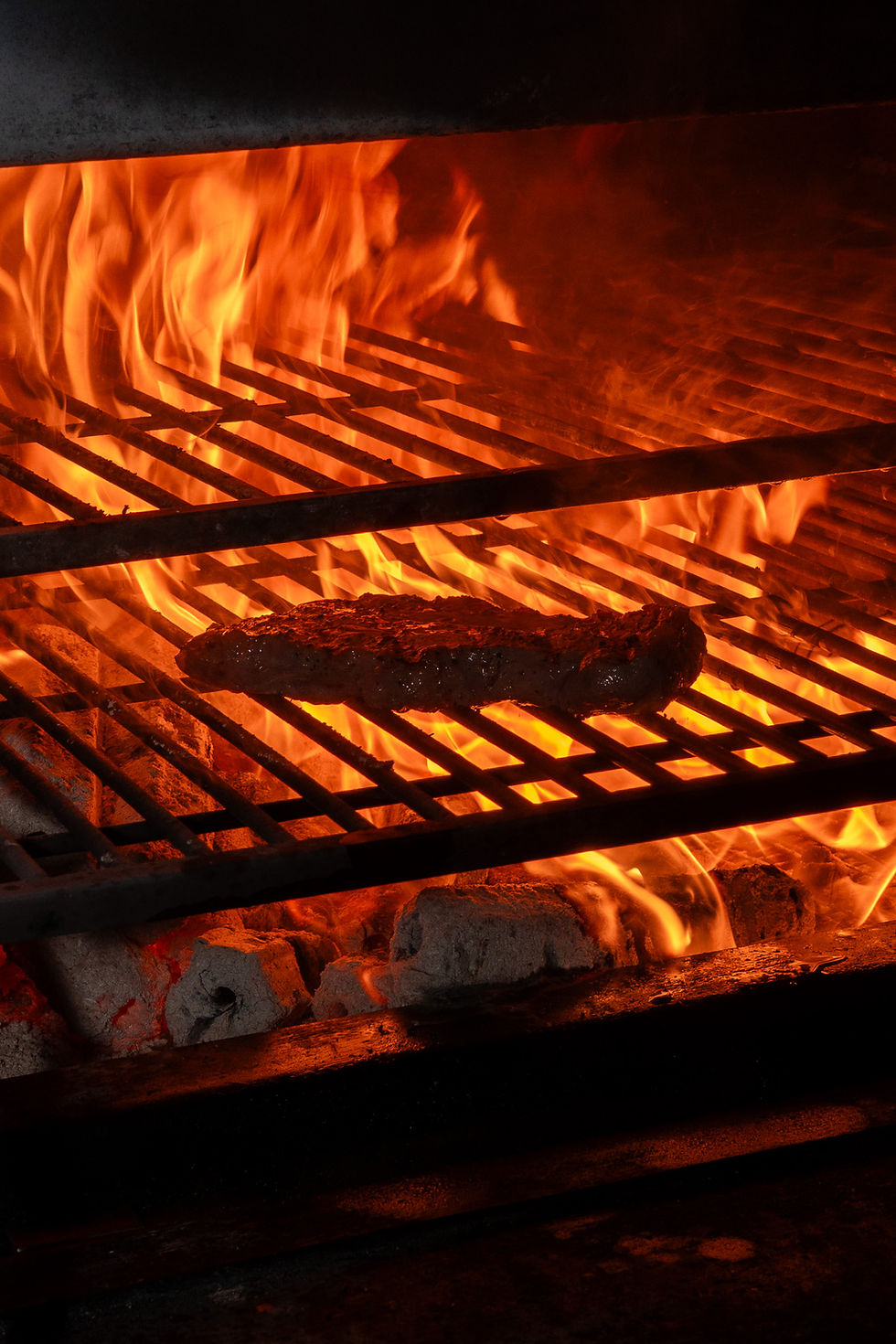 Meat sizzling on a grill over hot flames at south side keppel's woodfire dinner