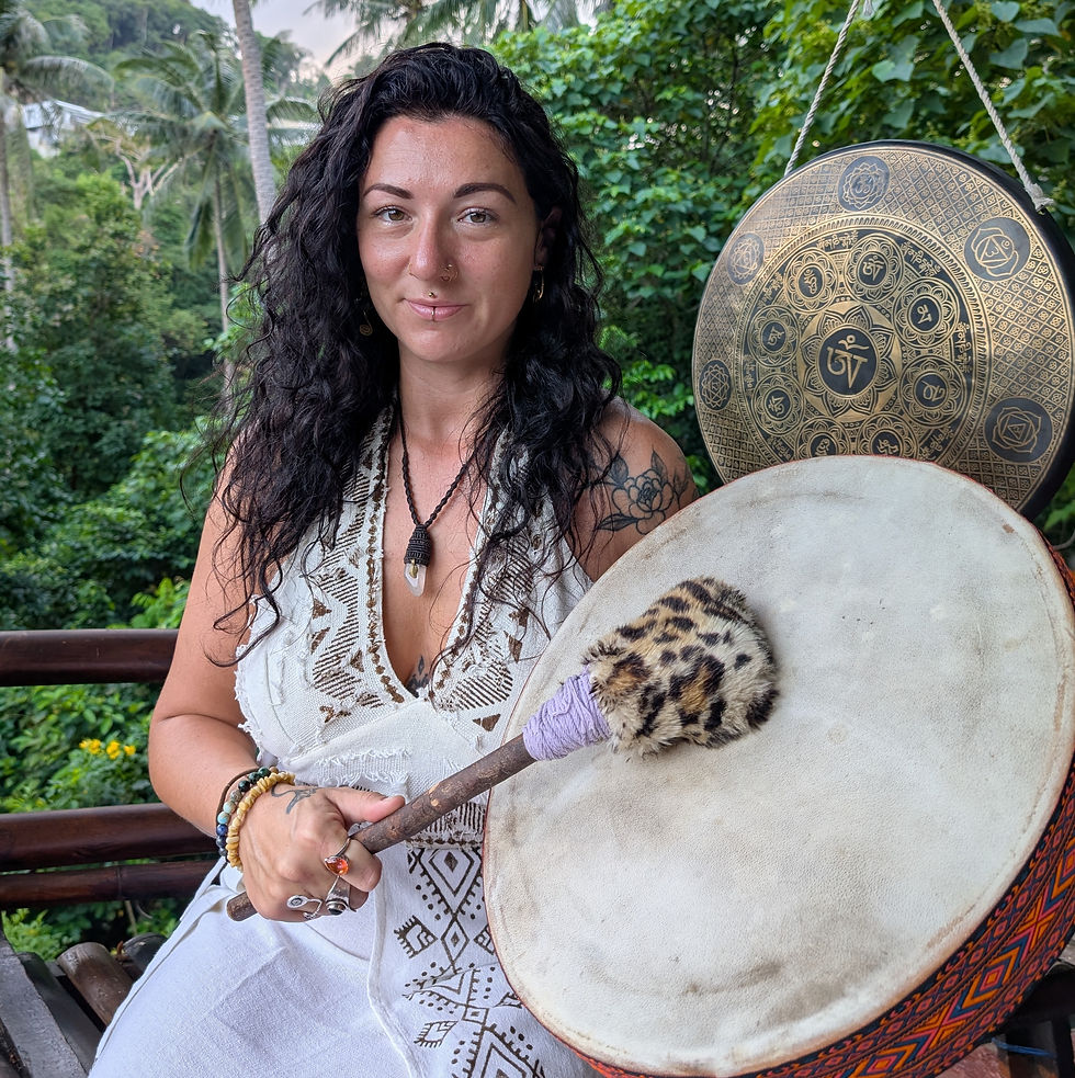 Woman in white dress holds a drumstick with a leopard-print tip in a lush, green setting. A decorative gong hangs in the background.