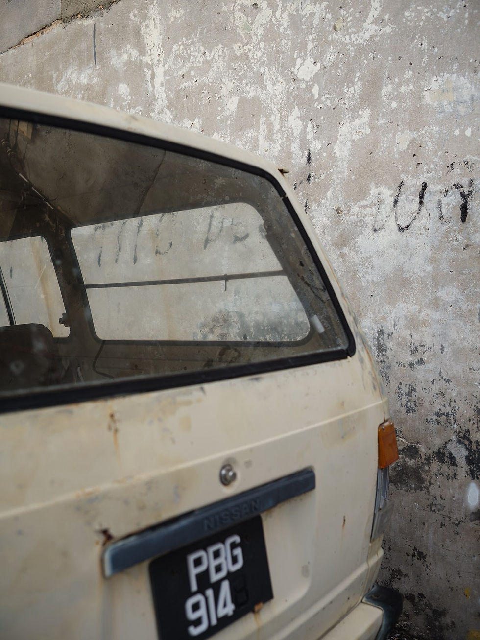 An old car’s back, paint faded and worn, sitting against an equally tired wall.