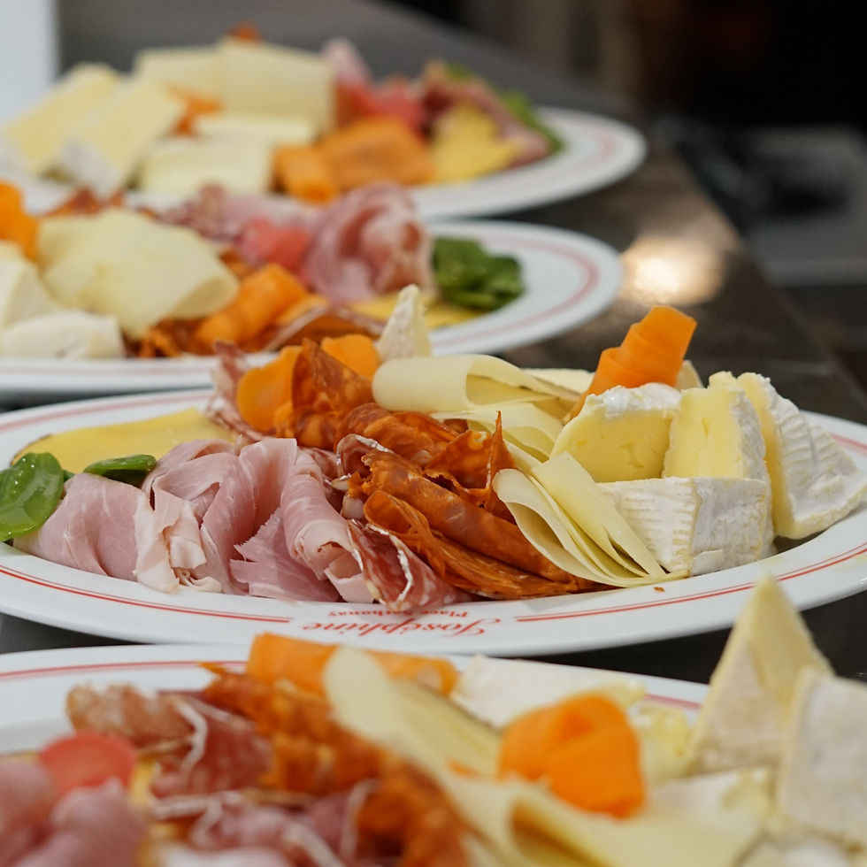 Assiettes de fromages et charcuteries, jambon, saucisson et légumes, dressées en file sur un comptoir; ambiance de dégustation.