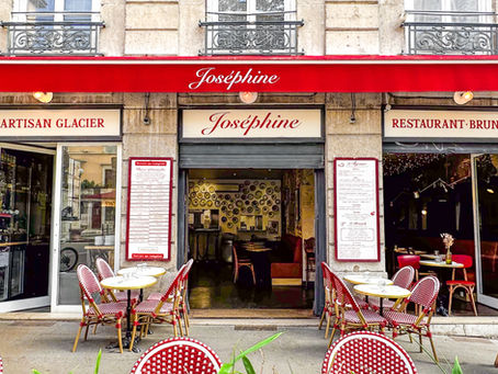 Façade d’un café-restaurant Joséphine, terrasse vide avec chaises rouges et blanches, enseigne artisan glacier, ambiance chic.