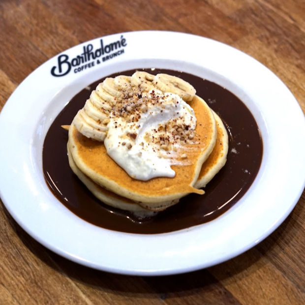 Pancakes garnis de banane et crème sur une assiette blanche Bootholmé Coffee & Brunch, sur table en bois.