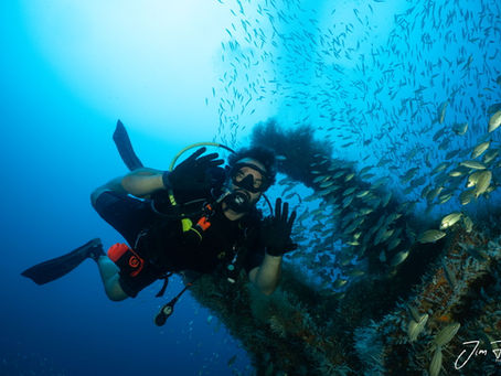 A confident scuba diver giving the ok hand signal underwater with the U-352 Submarine in the the background