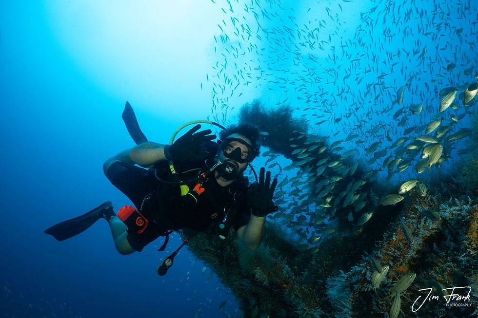 A confident scuba diver giving the ok hand signal underwater with the U-352 Submarine in the the background