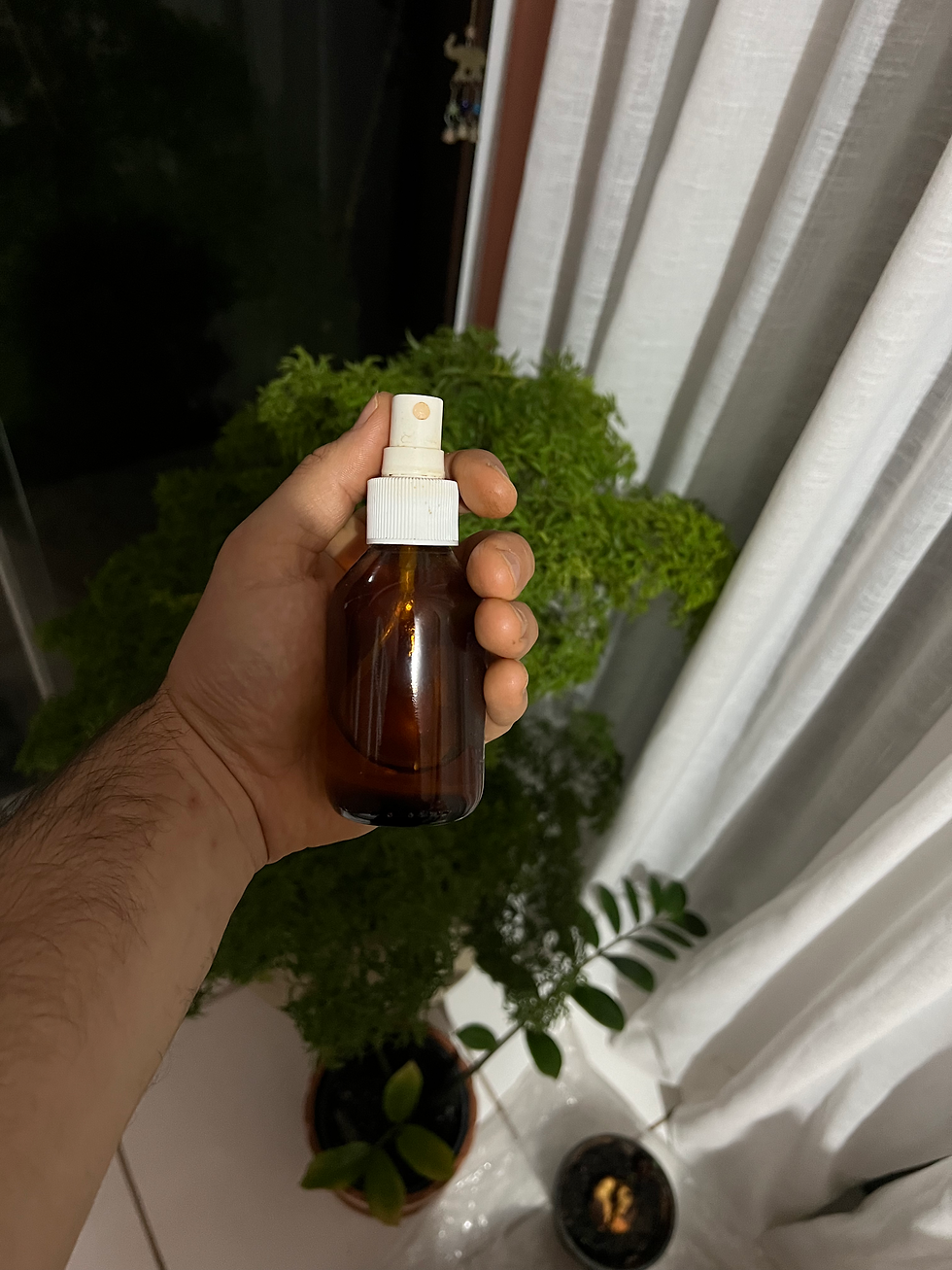 Mão com um pequeno frasco de spray em vidro colorido