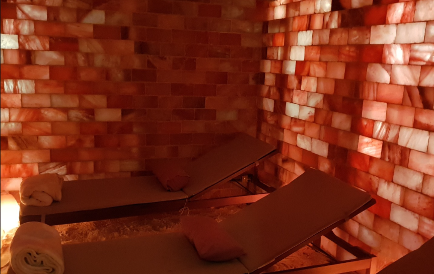 A calm Himalayan salt room with glowing pink salt brick walls, a salt crystal floor and two cushioned lounge chairs with blankets