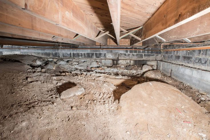 A dirt crawlspace with wooden beams overhead and concrete walls. The ground is uneven with rocks and dirt, creating a rustic, bare setting.