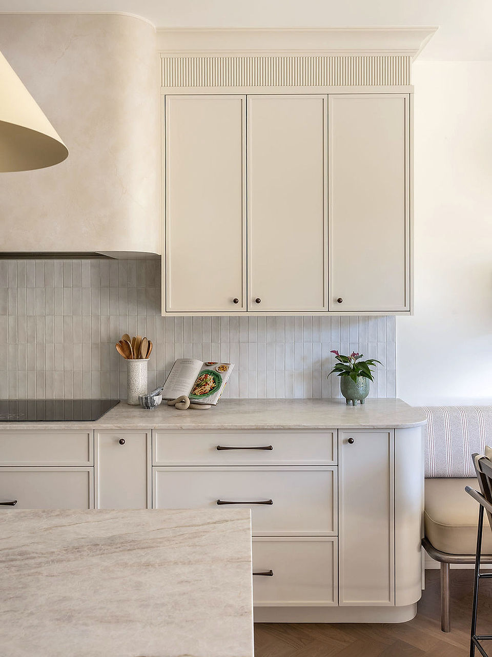 Cream shaker upper cabinets with fluted crown detail above marble countertop and curved banquette seating.