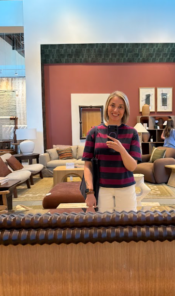 Interior designer taking a mirror selfie inside a High Point Market furniture showroom featuring warm earth tone sofas, layered rugs, and terracotta accent walls