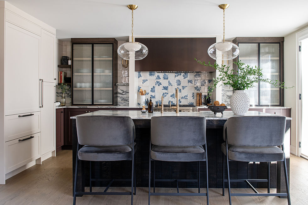 Modern transitional kitchen with dark wood cabinetry, marble island, and three upholstered bar stools; brass pendant lighting and blue patterned backsplash add contrast to the warm, layered interior.