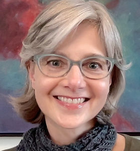 Headshot of Laura Schaffer from the shoulders up smiling wearing eyeglasses and a scarf.