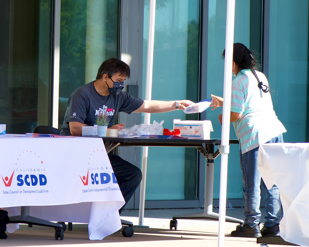 Thomas gives a bag of ten masks to someone outside of the Ed Roberts Campus.