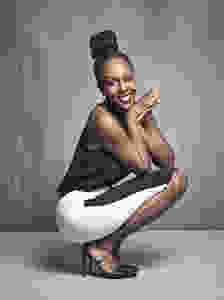 Stephanie Thomas squating and posing for the camera in a white skirt and black tank top shirt.