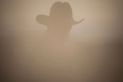 The silhouette of a man wearing a cowboy hat is nearly lost in the blur of a sandstorm.