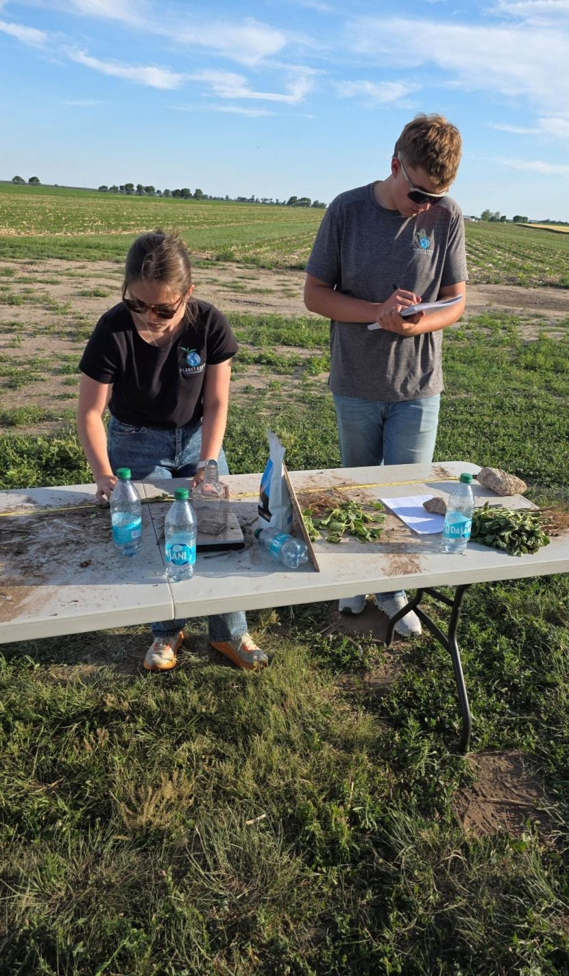 PEA team recording trial data for soybeans and take notes at a field table under a blue sky.