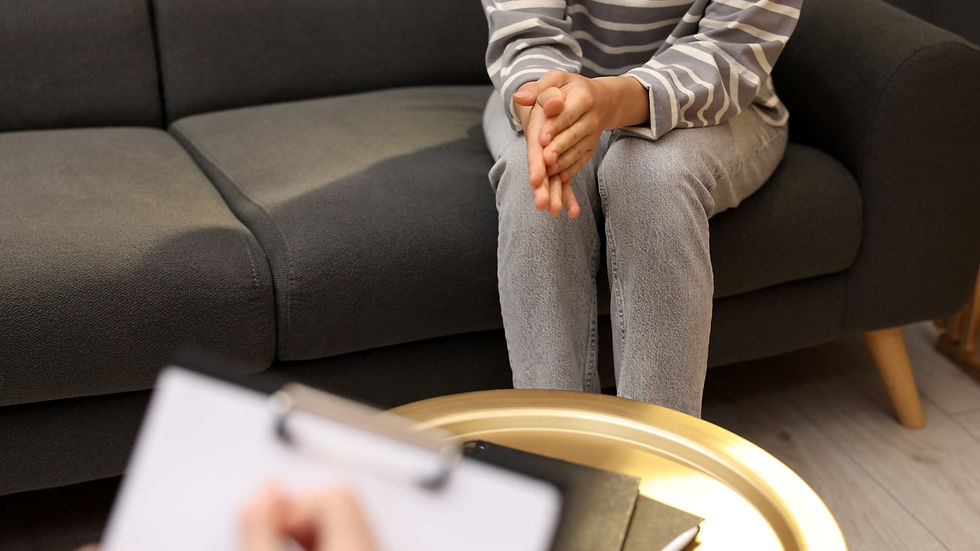 Person seated on couch with hands clasped, counselling setting