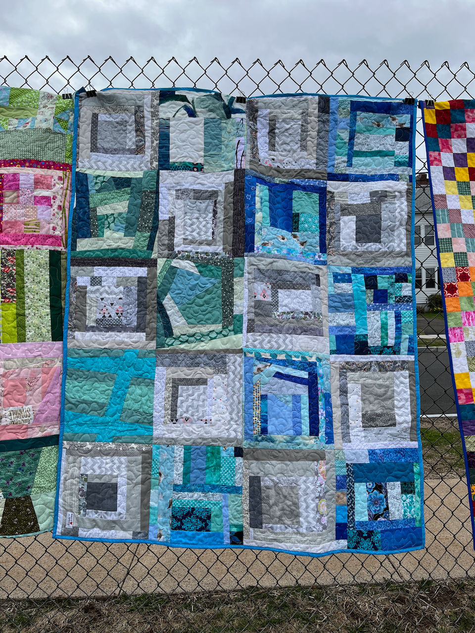 blue, green, gray improvisational quilt blocks hanging on a fence