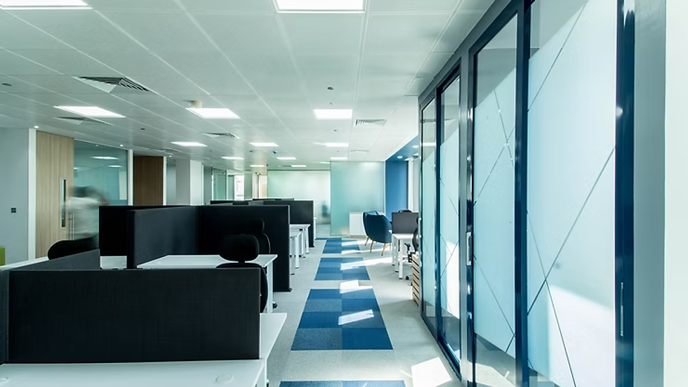 Bright open-plan office at Verod Capital with blue-accented carpet, ergonomic desks, and glass-partitioned meeting rooms in a corporate workspace.