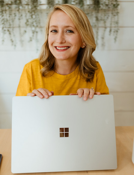 A woman smiling, wearing a yellow shirt and holding a laptop
