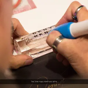 הקליגרף יורם קפלן בזמן חריטה ידנית על בקבוק בושם DKNY Stories בהתאמה אישית, פרסונליזציה יוקרתית לבישום פרימיום במהלך אירוע מותג