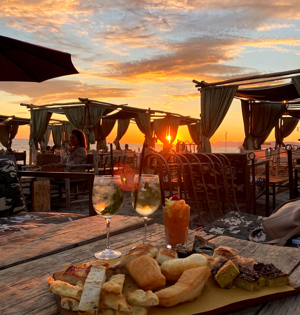 Sonnenuntergang am Meer, gedeckter Holztisch mit Gebäck und drei Getränken. Menschen in Pavillons im Hintergrund, entspannte Atmosphäre. Strand der Versilia in Forte dei marmi