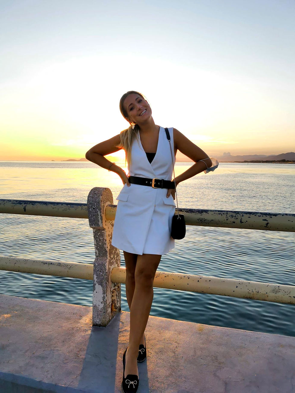 Fiona Ulrich in weißem Kleid lehnt lächelnd an Geländer, Sonnenuntergang am Meer im Hintergrund, entspannte Stimmung, klare Himmel, Wasser.
AUf dem Ponte in Forte dei Marmi