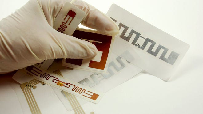 A hand, wearing a medical glove, holds several RFID tags.