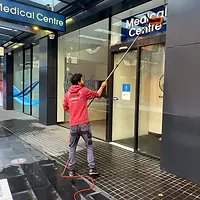 In Perth, a Zavvers cleaning professional in a branded pink shirt is engaged in exterior cleaning at a Medical Centre. Using an extended water-fed pole to reach high windows, the cleaner works diligently to ensure the entrance area is spotless and inviting, reflecting Zavvers' expertise in maintaining commercial exteriors.