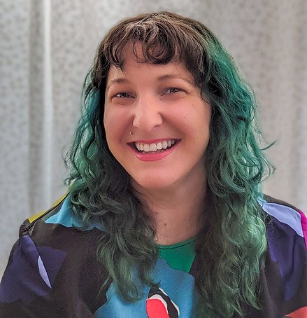 Portrait of Tracy Gabrys with long, wavy teal hair and a bright smile, wearing a colorful patterned top.