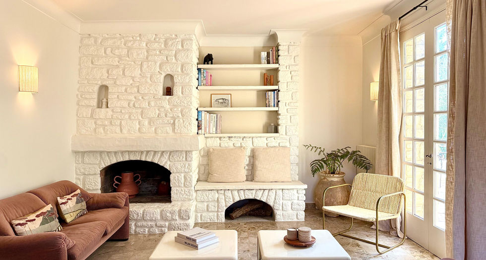 Salon spacieux avec canapé, cheminée blanche et grandes ouvertures sur l'extérieur.