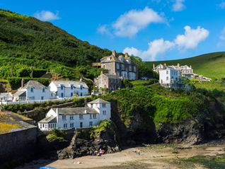 Port Isaac village, Cornwall, with white-painted cottages and stone houses clustered on rocky hillsides above a small sandy beach.