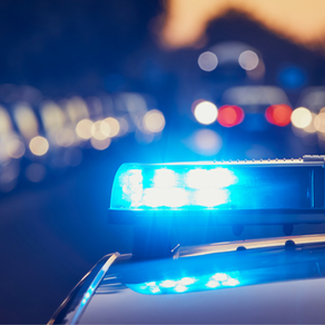 Police car with blue lights flashing in a blurred urban street at dusk. The scene is energetic with a focus on emergency response.