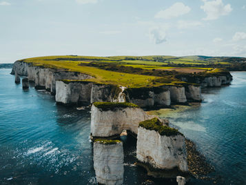 Clifftop landscape with white chalk cliffs and turquoise sea. Green grassy fields and blue sky with clouds create a serene atmosphere.