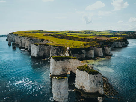Clifftop landscape with white chalk cliffs and turquoise sea. Green grassy fields and blue sky with clouds create a serene atmosphere.