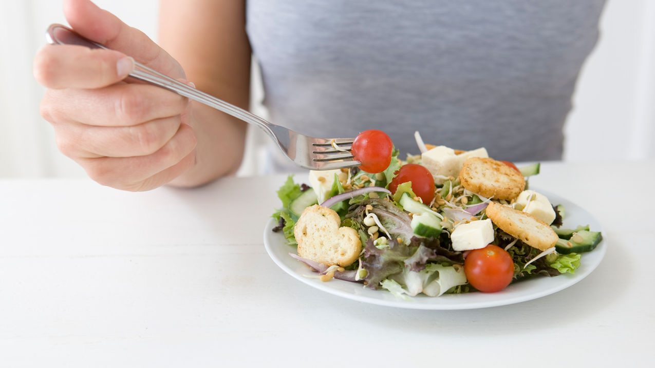 mão segurando garfo e um prato saboroso de legumes