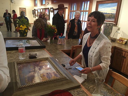 artist lindy cook severns with framed painting and clients at gallery counter