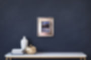 Silver framed snow scene on dark wall above white table with pottery