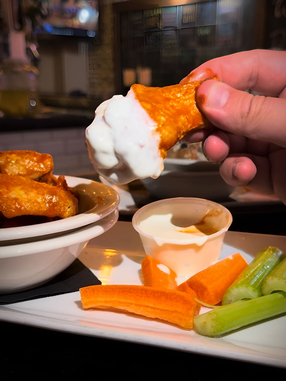 Buffalo wing dipped in ranch at Smithtown Bistro & Pub with carrots, celery, and sauce—Super Bowl favorite on Long Island.
